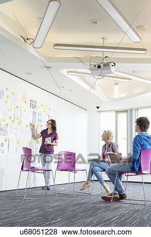 Stock Photo - Creative businesswoman giving presentation to colleagues in office. Fotosearch