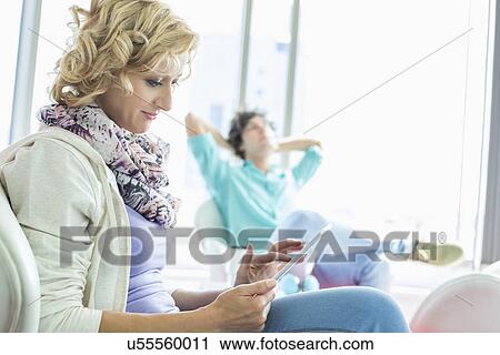 Stock Image - Creative businesswoman using digital tablet at lobby with colleague relaxing in background. Fotosearch