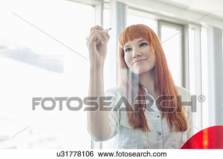 Stock Photograph - Creative businesswoman writing on glass wall in office. Fotosearch