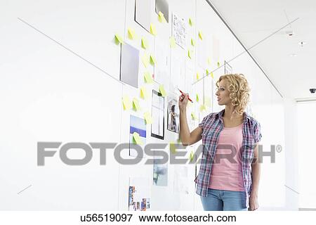 Stock Photo - Creative businesswoman writing on sticky paper in office. Fotosearch