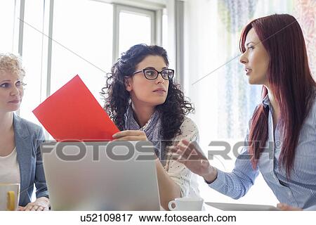 Stock Photo - Creative businesswomen discussing in meeting at office. Fotosearch