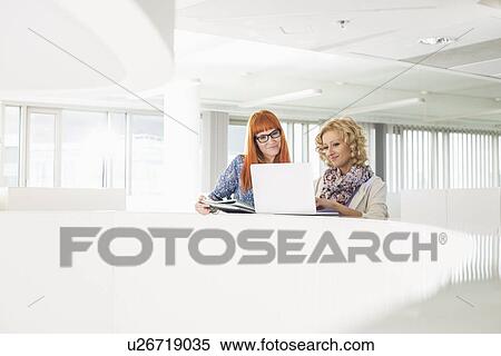 Creative businesswomen using laptop together in office View Large Photo Image Stock Photography - Creative businesswomen using laptop together in office. Fotosearch