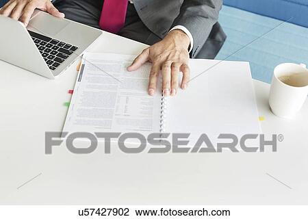 Stock Image - Cropped image of businessman with book and laptop at desk. Fotosearch