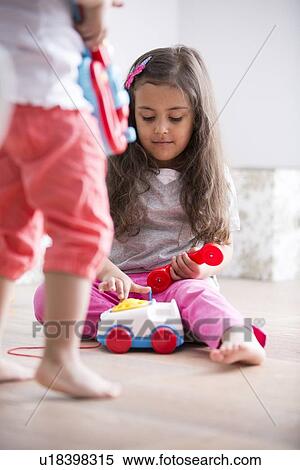 Stock Photography - Cute girl dialing the toy telephone while playing with sister at home. Fotosearch