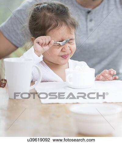 Cute girl making face while having cream with father at home View Large Photo Image Stock Image - Cute girl making face while having cream with father at home. Fotosearch
