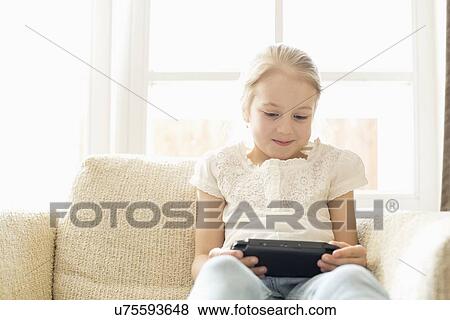 Cute girl playing hand-held video game at home View Large Photo Image Stock Photo - Cute girl playing hand-held video game at home. Fotosearch