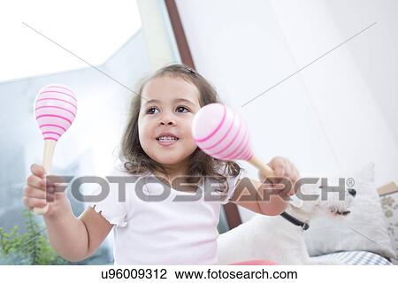 Stock Image - Cute girl playing with maracas while sitting beside dog at home. Fotosearch