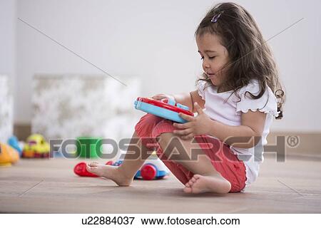 Stock Photo - Cute girl playing with toy guitar at home. Fotosearch