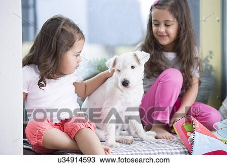 Stock Image - Cute girls with puppy sitting on bed. Fotosearch