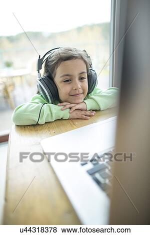 Stock Photo - Cute little girl listening to music on headphones while using laptop at home. Fotosearch