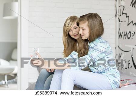 Picture - Cute sisters photographing themselves through cell phone at home. Fotosearch