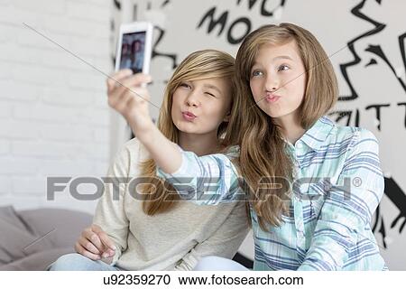 Cute sisters pouting while taking photos with smart phone at home View Large Photo Image Stock Image - Cute sisters pouting while taking photos with smart phone at home. Fotosearch