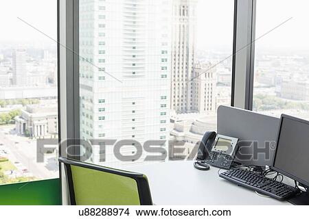 Desktop computer and landline phone on desk by glass window in office View Large Photo Image Picture - Desktop computer and landline phone on desk by glass window in office. Fotosearch