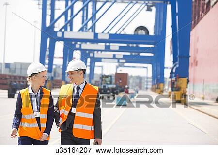 Engineers conversing while walking in shipping yard View Large Photo Image Stock Photo - Engineers conversing while walking in shipping yard. Fotosearch