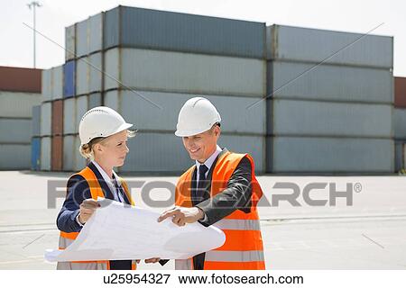 Engineers looking at blueprint in shipping yard View Large Photo Image Stock Photo - Engineers looking at blueprint in shipping yard. Fotosearch