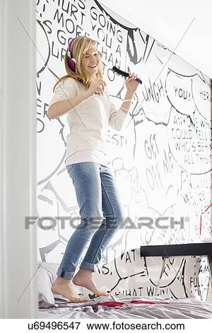 Excited girl listening music while singing into hairbrush at home View Large Photo Image Stock Photo - Excited girl listening music while singing into hairbrush at home. Fotosearch