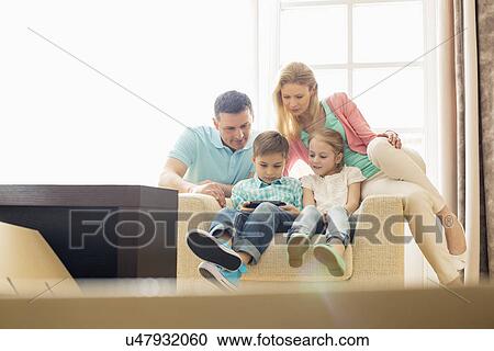 Family looking at boy playing hand-held video game at home View Large Photo Image Stock Image - Family looking at boy playing hand-held video game at home. Fotosearch
