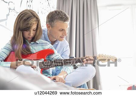 Stock Photo - Father and daughter playing electric guitar at home. Fotosearch