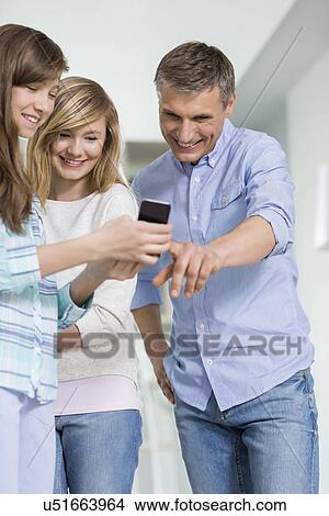 Father and daughters using smart phone at home View Large Photo Image Picture - Father and daughters using smart phone at home. Fotosearch