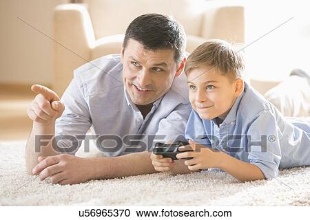 Stock Image - Father and son playing video game on floor at home. Fotosearch