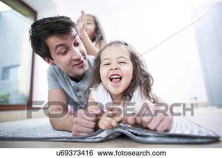 Father looking at cheerful daughter lying on blanket at home View Large Photo Image Stock Photograph - Father looking at cheerful daughter lying on blanket at home. Fotosearch