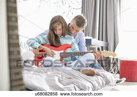 Stock Photo - Father teaching daughter to play guitar at home. Fotosearch