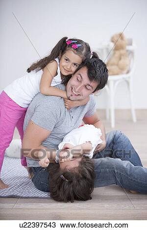 Stock Image - Father with playful daughters at home. Fotosearch