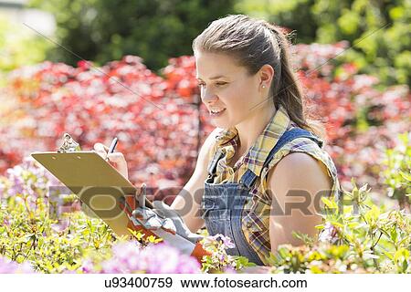 Stock Photo - Female supervisor writing on clipboard in garden. Fotosearch