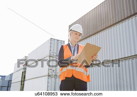 Stock Image - Female worker reading clipboard in shipping yard. Fotosearch