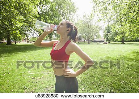 Fit woman drinking water while listening to music in park View Large Photo Image Stock Image - Fit woman drinking water while listening to music in park. Fotosearch