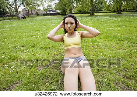 Stock Image - Fit woman looking away while performing sit-ups at park. Fotosearch