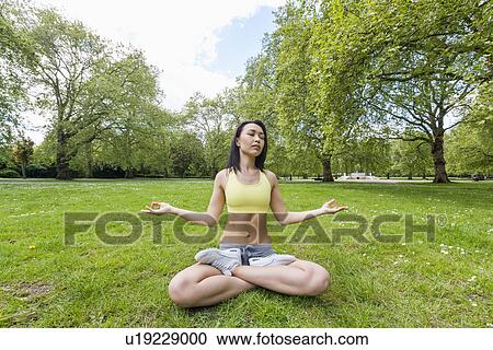 Stock Image - Full length of beautiful fit woman performing yoga at park. Fotosearch