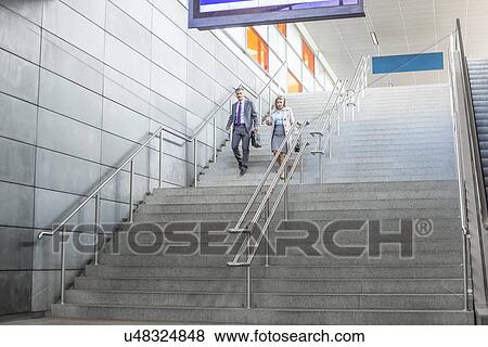 Full length of businessman and businesswoman walk down stairs at railway station View Large Photo Image Stock Photo - Full length of businessman and businesswoman walk down stairs at railway station. Fotosearch