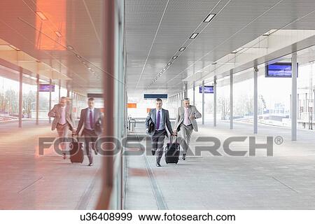 Stock Photo - Full length of businessmen with luggage rushing on railroad platform. Fotosearch