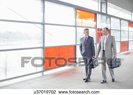 Stock Image - Full length of businessmen with briefcase walking in railroad station. Fotosearch