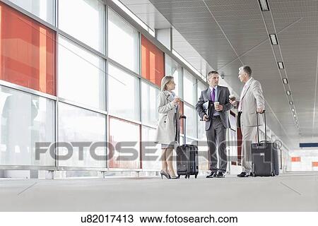 Stock Image - Full length of businesspeople with luggage talking on railroad platform. Fotosearch