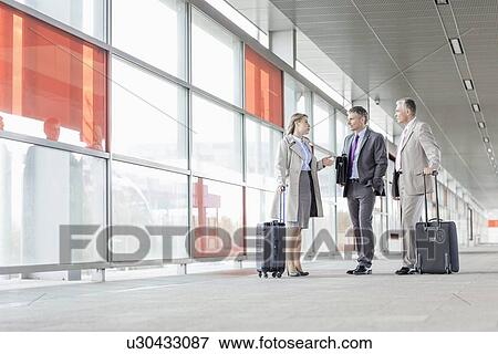 Stock Photo - Full length of businesspeople with luggage talking on railroad platform. Fotosearch