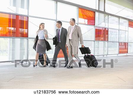 Stock Photograph - Full length of businesspeople with luggage walking on railroad platform. Fotosearch