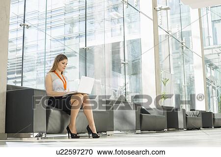 Full-length of businesswoman using laptop at office lobby View Large Photo Image Stock Image - Full-length of businesswoman using laptop at office lobby. Fotosearch