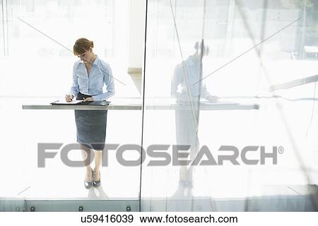 Full-length of businesswoman writing on document in office View Large Photo Image Stock Photo - Full-length of businesswoman writing on document in office. Fotosearch