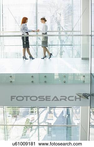 Stock Image - Full-length of businesswomen conversing in office. Fotosearch