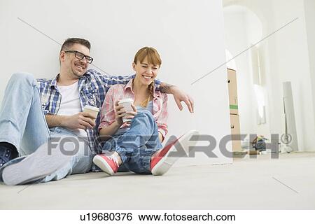 Stock Photograph - Full-length of cheerful couple with coffee cups in new house. Fotosearch