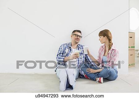 Stock Image - Full-length of couple having coffee in new house. Fotosearch