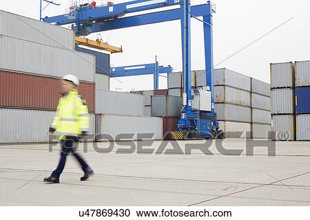 Stock Image - Full-length of female worker walking in shipping yard. Fotosearch