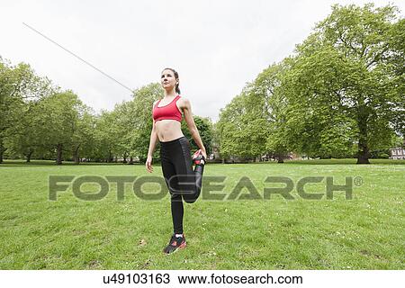 Stock Image - Full length of fit young woman performing stretching exercise in park. Fotosearch