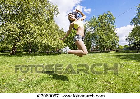 Full length of happy fit woman jumping in park View Large Photo Image Stock Photo - Full length of happy fit woman jumping in park. Fotosearch