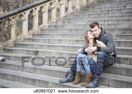 Stock Image - Full length of loving woman kissing man while sitting on steps outdoors. Fotosearch