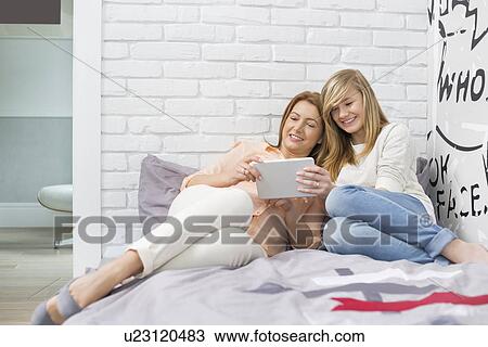 Stock Image - Full-length of mother with daughter using tablet PC in bedroom. Fotosearch