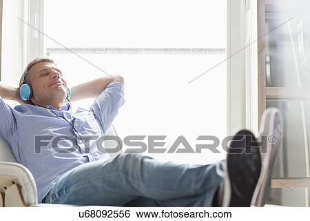 Stock Photograph - Full-length of relaxed Middle-aged man listening to music at home. Fotosearch