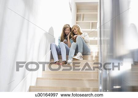 Full-length of sisters listening to music on stairway View Large Photo Image Stock Photo - Full-length of sisters listening to music on stairway. Fotosearch